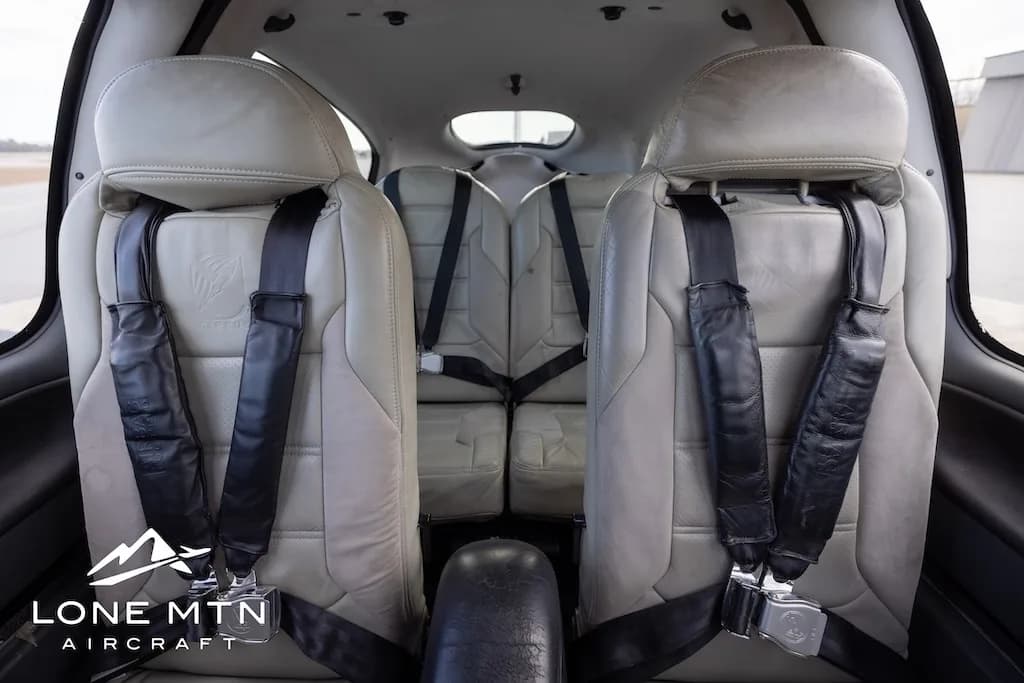A view of the four light-colored leather seats with black seatbelts inside the aircraft cabin.
