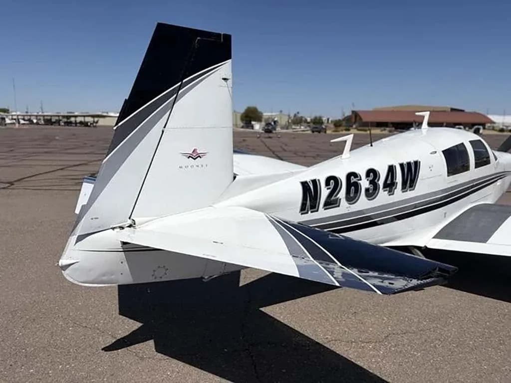 A rear-side view of the white Mooney M20 aircraft N2634W, highlighting its tail with black and grey stripes.