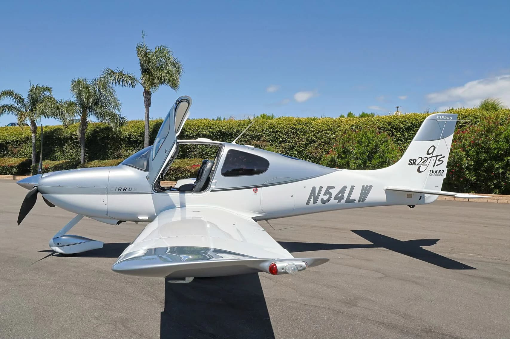 Side view of a silver and white Cirrus SR22T (N54LW) with both doors open, parked on an tarmac.