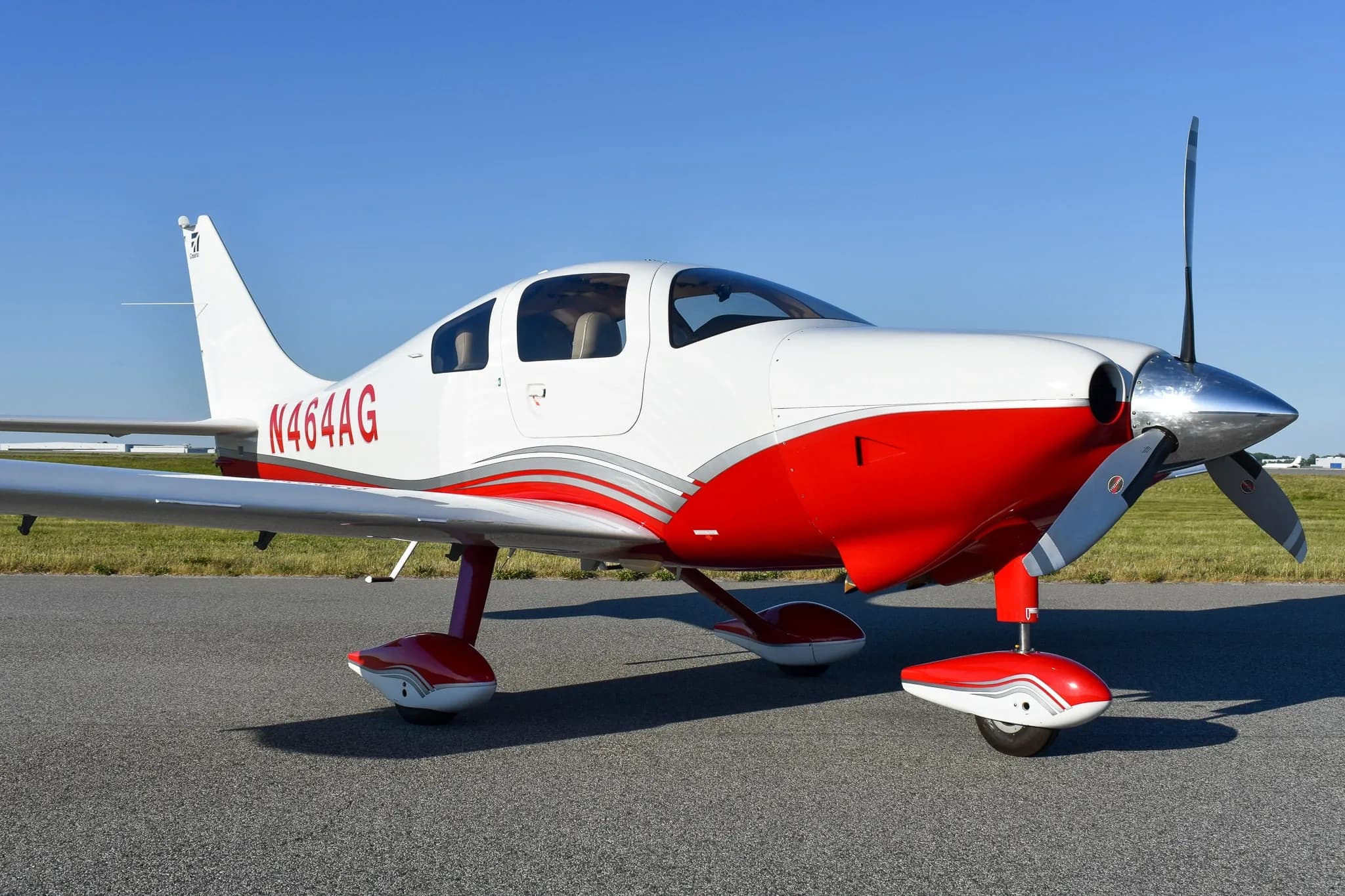 A front-side view of the white and red Cirrus SR22 aircraft, registration N464AG, parked on an airfield.