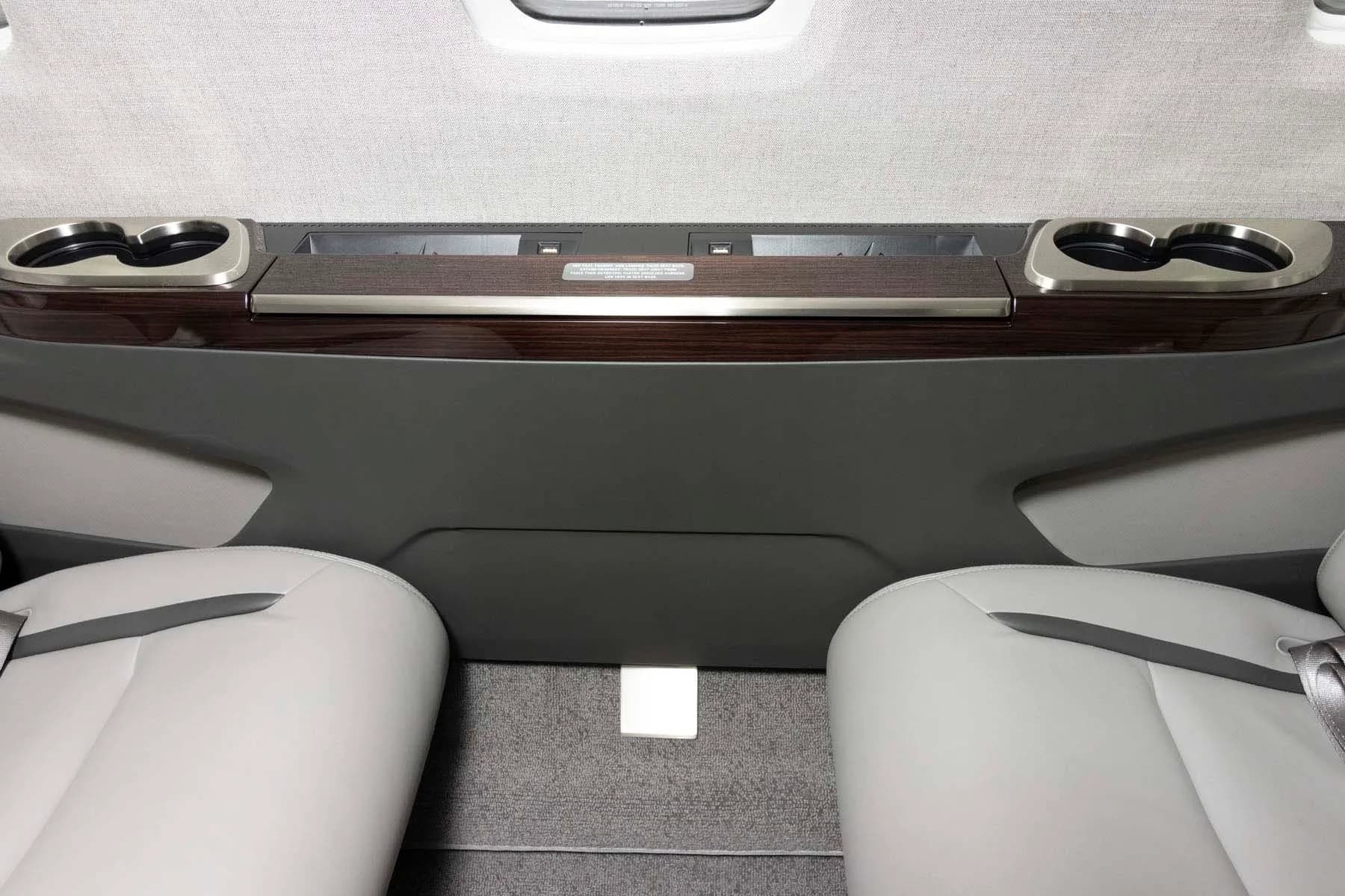 A close-up view of the private jet's cabin side panel with cup holders and a dark wood trim.