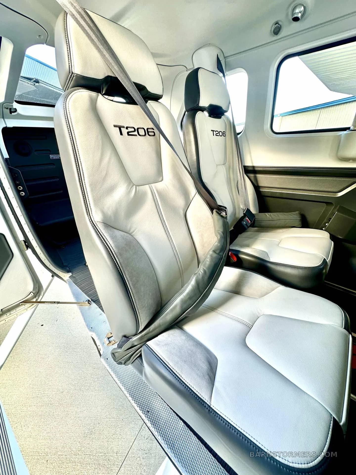 The interior of a Cessna T206 shows light gray and black leather seats with "T206" embroidered on the headrests.