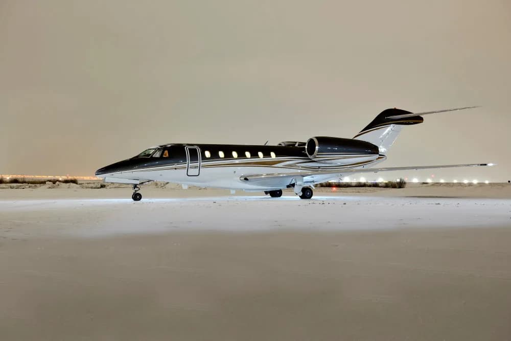 A Citation CJ3 aircraft on a snowy tarmac at night.