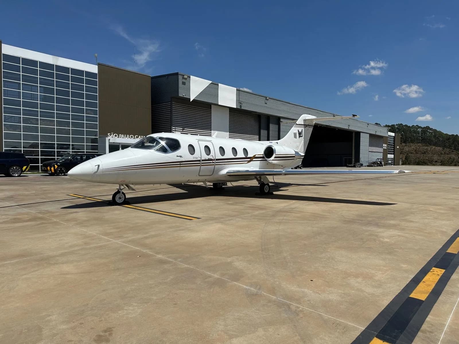 A white business jet with brown stripes and a 'W' tail logo is parked on a tarmac in front of a hangar under a clear blue sky.