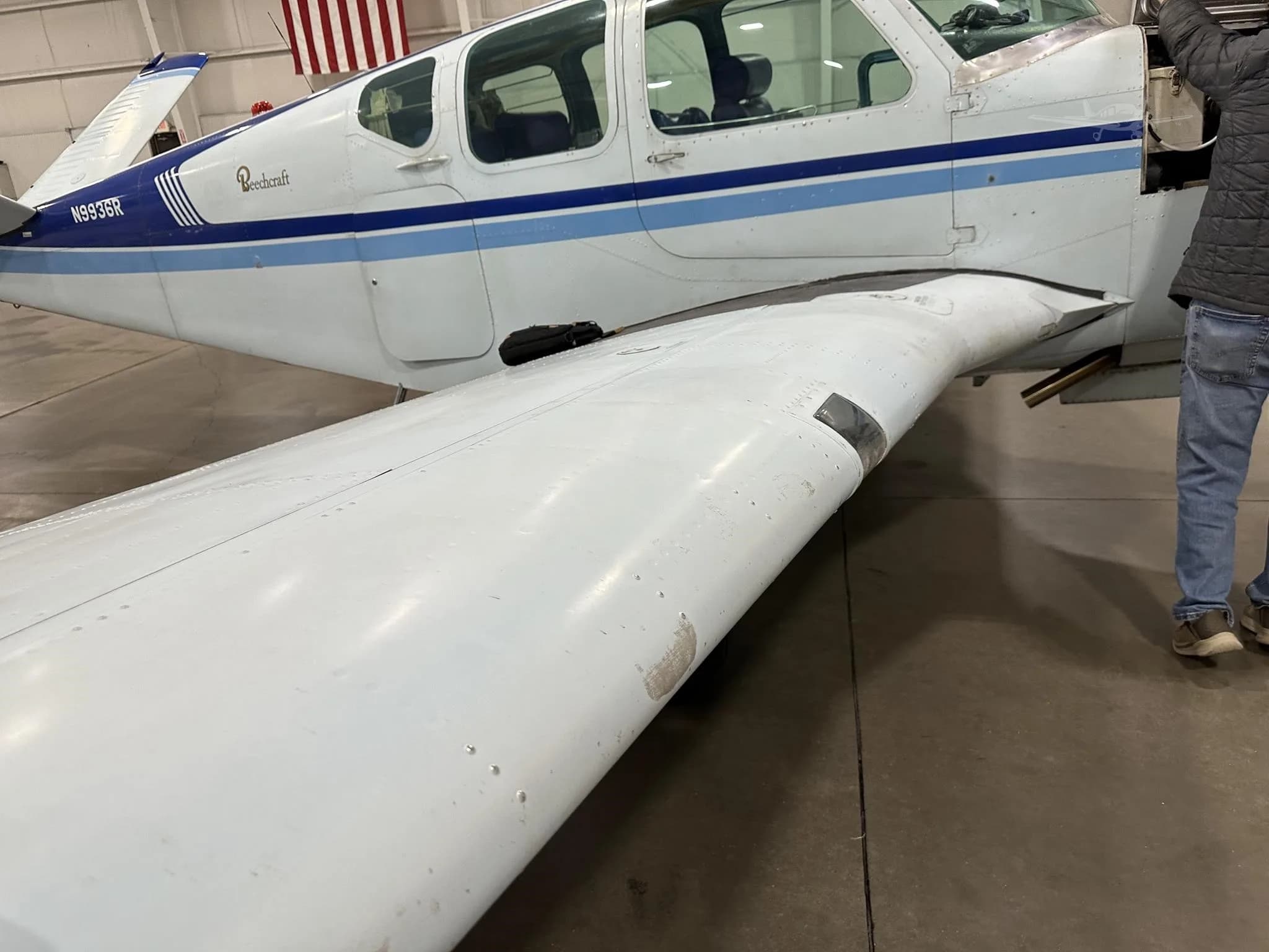 A close-up view of the white wing and fuselage of the Beechcraft Bonanza N9936R, with a person standing nearby.