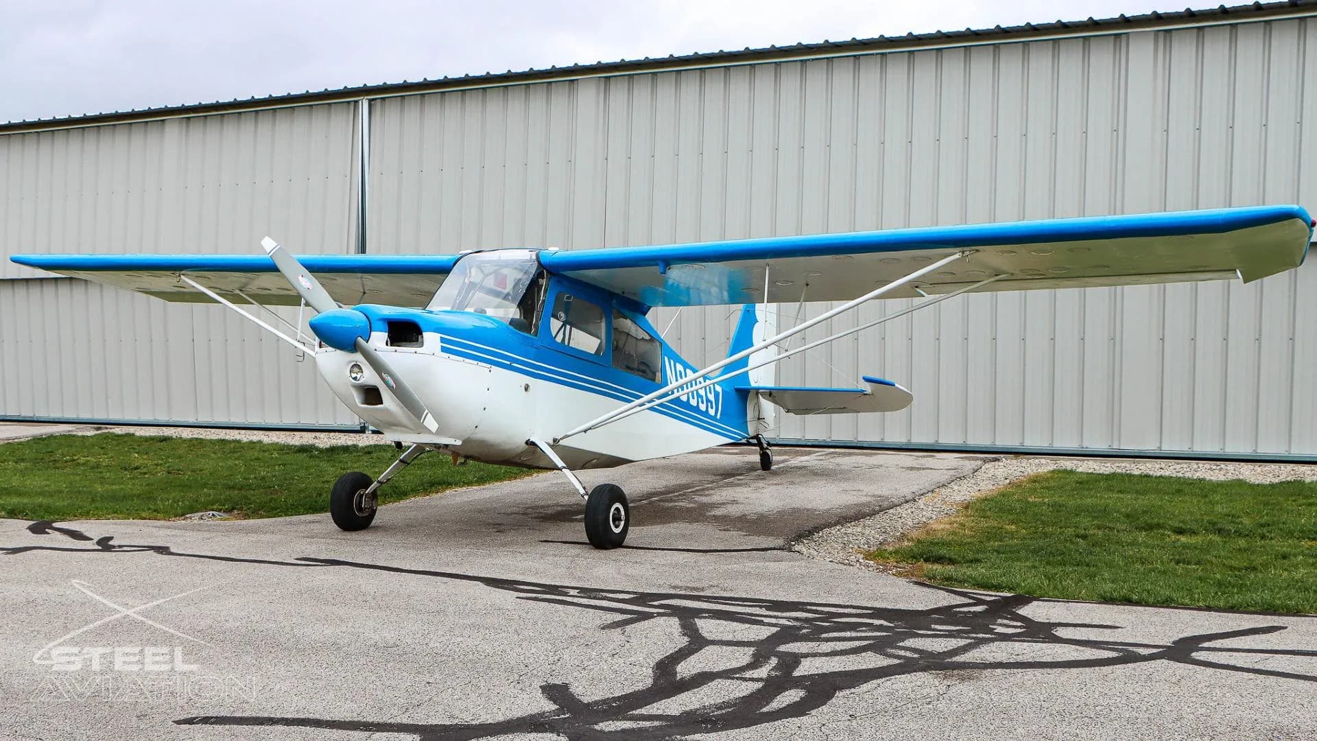 Front three-quarter view of a white and blue Bellanca 7GCBC Citabria aircraft with registration N90997, parked on an asphalt ramp.