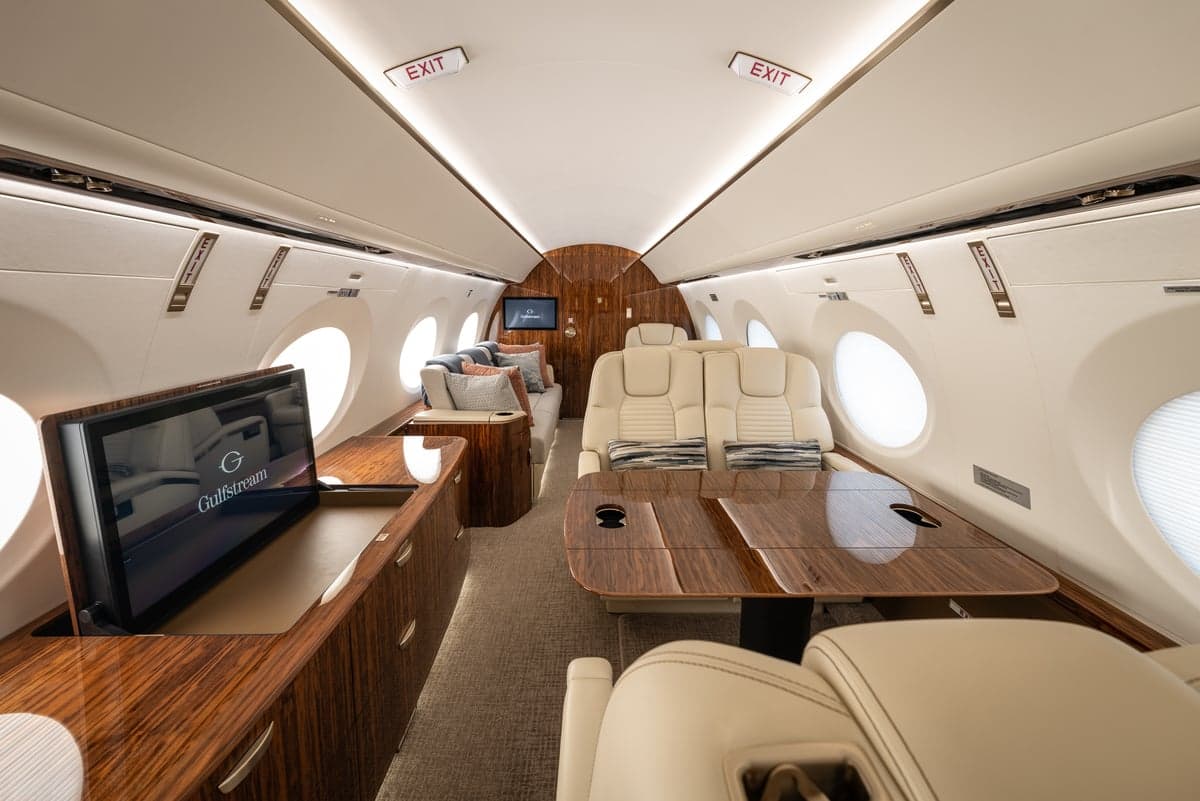 The aircraft's interior includes a seating area, entertainment system, and wood cabinetry.