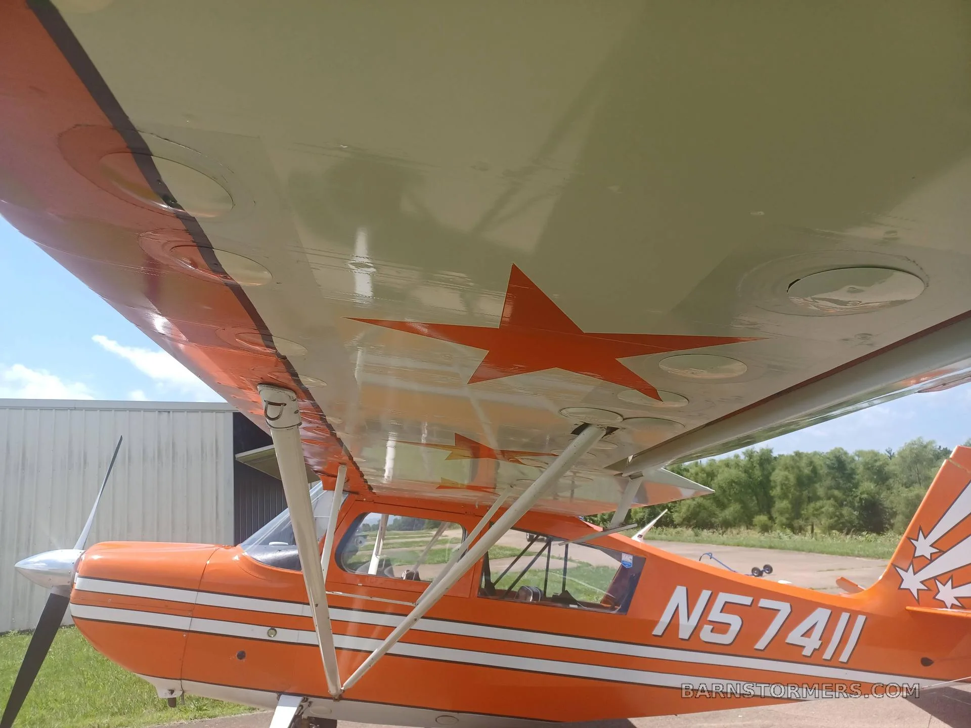 A view looking up at the underside of the orange and white aircraft's wing, showing a red star decal and registration N57411.