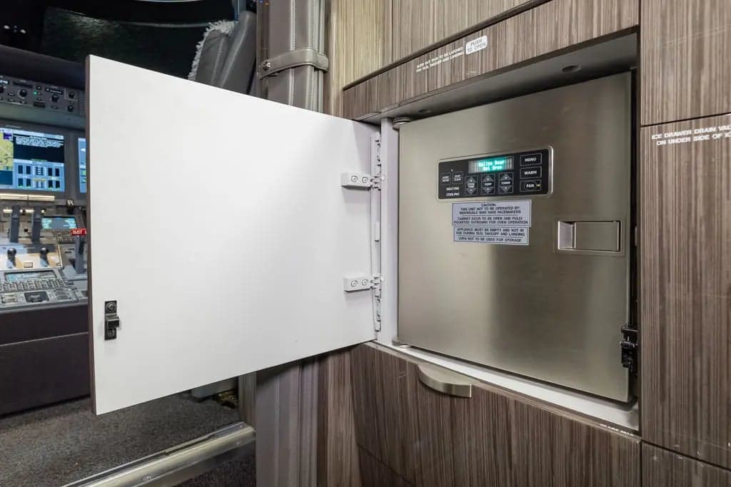 Interior view of the aircraft galley with an open refrigerator and cockpit in the background.
