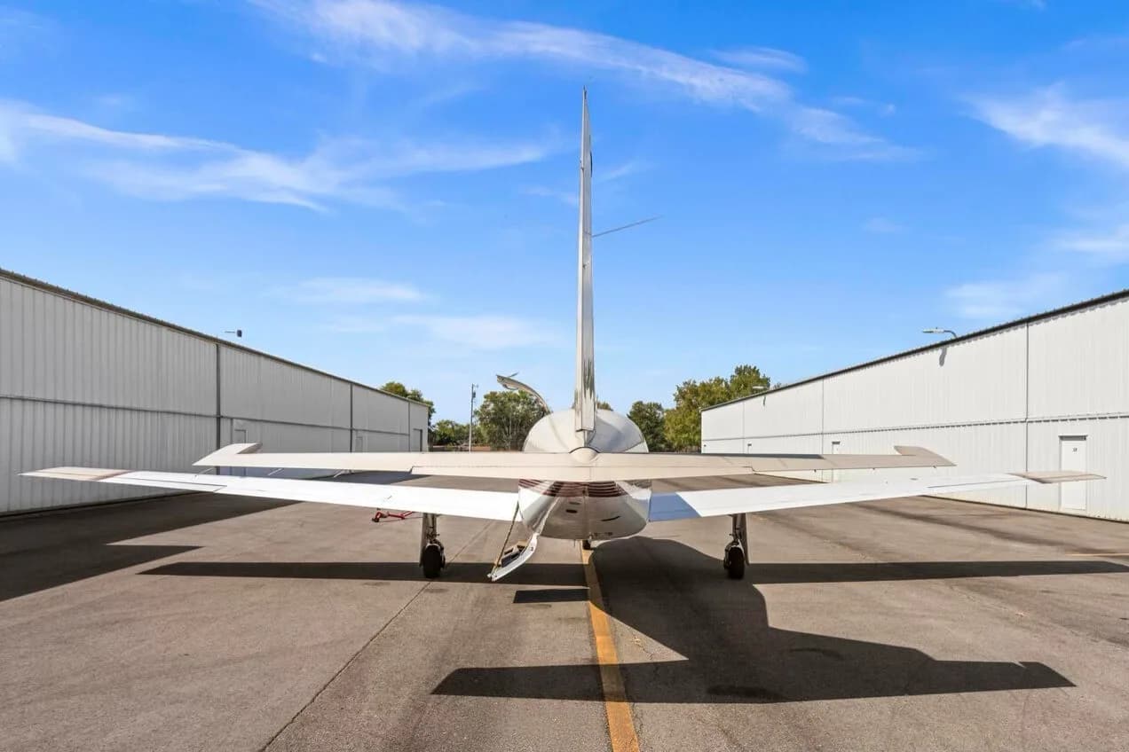 A rear view of the Piper Malibu N31BX, showing its tail and wings, parked on an airfield between hangars.