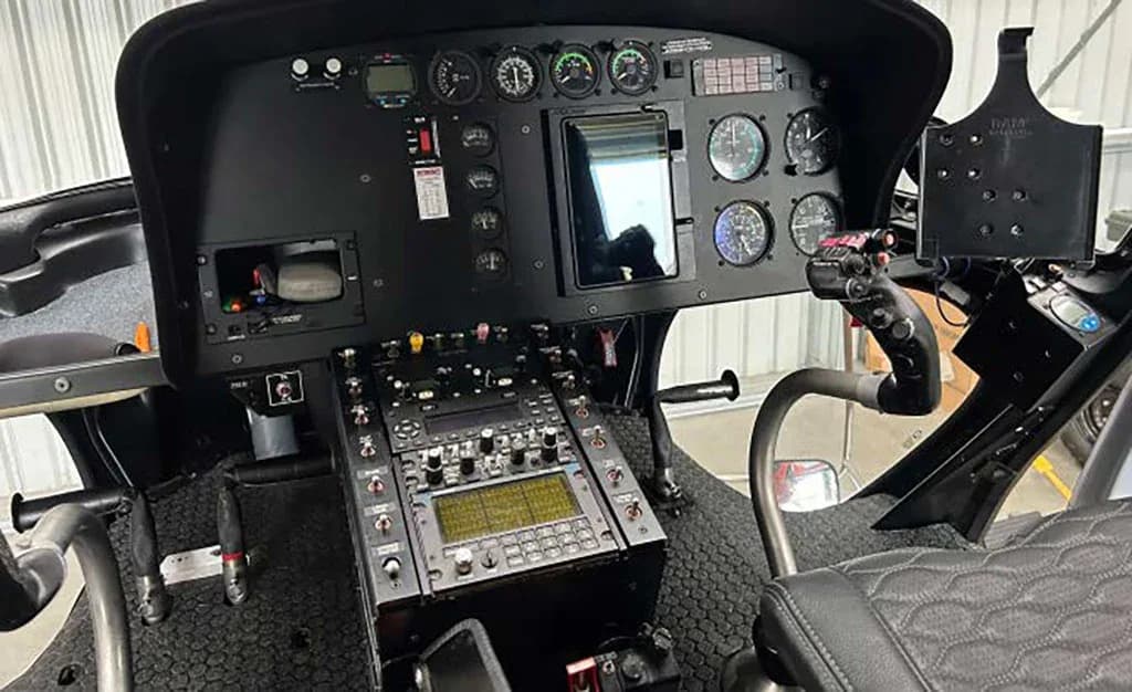 A close-up view of a helicopter's instrument panel and central control console with various gauges and screens.