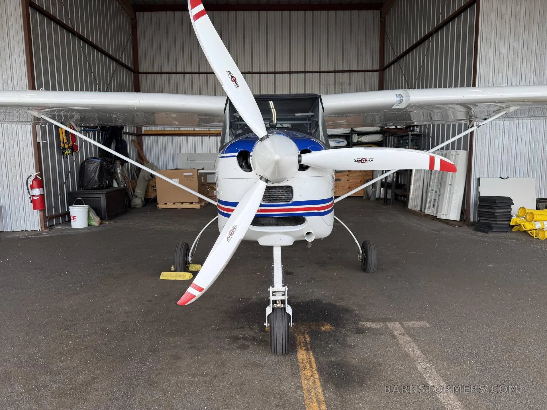 A front view of the white Tecnam P92 Echo Super light sport aircraft with a three-bladed propeller, parked in a hangar.