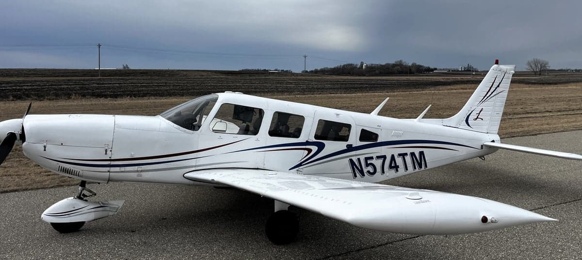 Side view of a white Piper PA-28-181 Archer II aircraft with registration N574TM on an airfield.