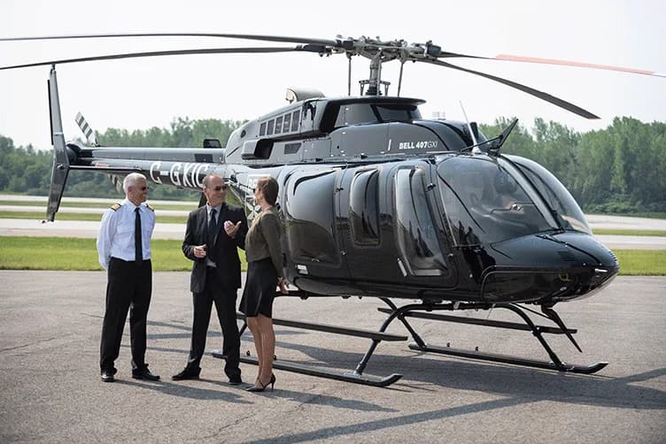 A black Bell 407 GXi helicopter with people standing nearby.