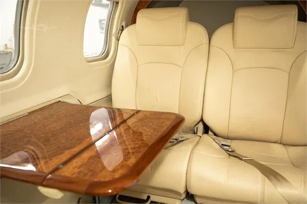 The aircraft's interior cabin features two tan leather seats and a polished wooden fold-out table.