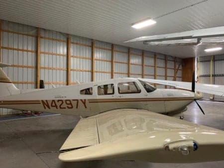 A cream-colored single-engine propeller aircraft with brown stripes is parked in a hangar.