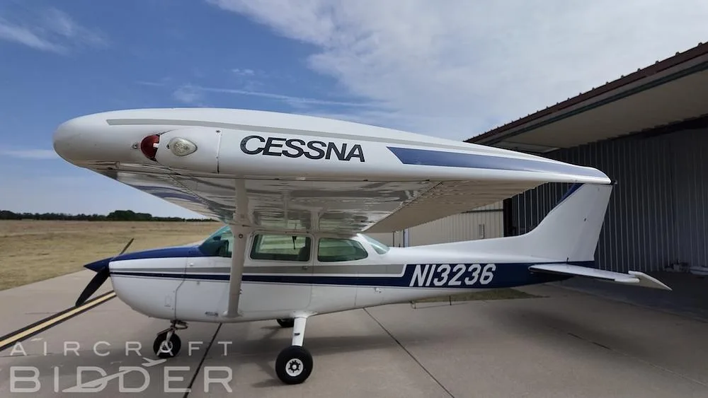 A side view of a white and blue Cessna 172 Skyhawk (N13236) with 'CESSNA' on the wing, parked on an airfield.