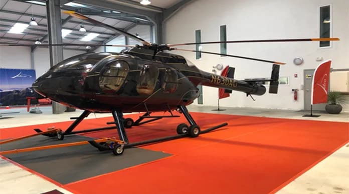 A black helicopter sits on a red carpet in a hangar.