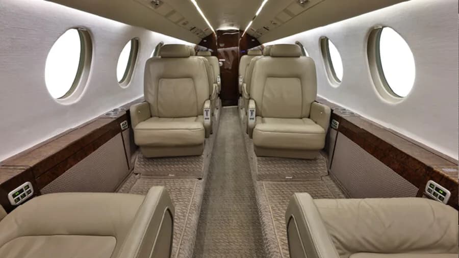 The luxurious cabin interior of a business jet featuring beige leather seats and large windows.