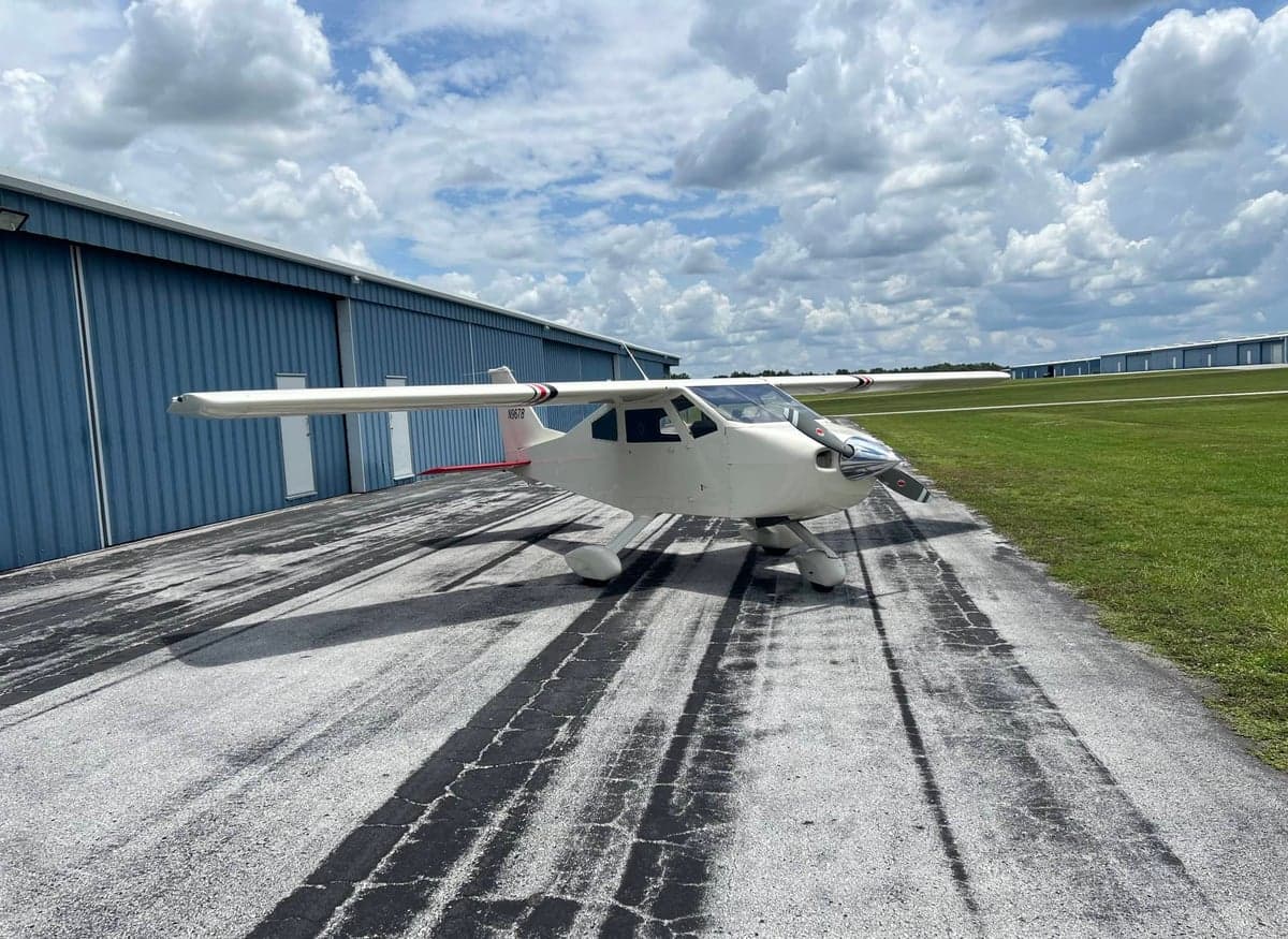 A white aircraft parked on the tarmac in front of a blue building.