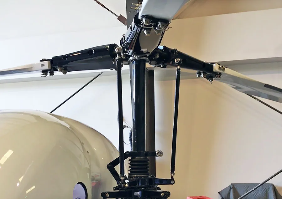 Close-up view of the main rotor head and blades of a white helicopter inside a hangar.