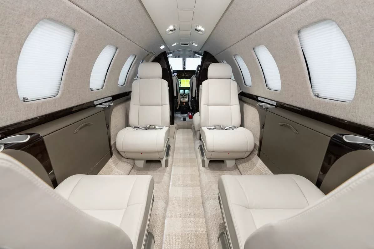 The private jet cabin interior with light-colored seats and a view towards the cockpit through the open door.