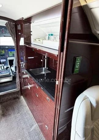 The aircraft's galley area featuring a sink, dark countertops, and wood cabinetry, with the cockpit visible in the background.