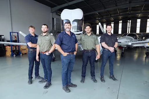 Five men stand in a hangar in front of a white Diamond DA42 twin-engine aircraft.