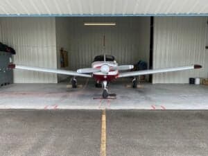 Front view of a maroon and white single-engine aircraft parked in a hangar.