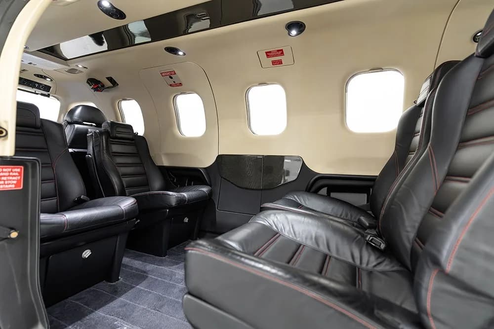 A view of the TBM 930 cabin interior, showing multiple rows of black leather seats with red stitching.