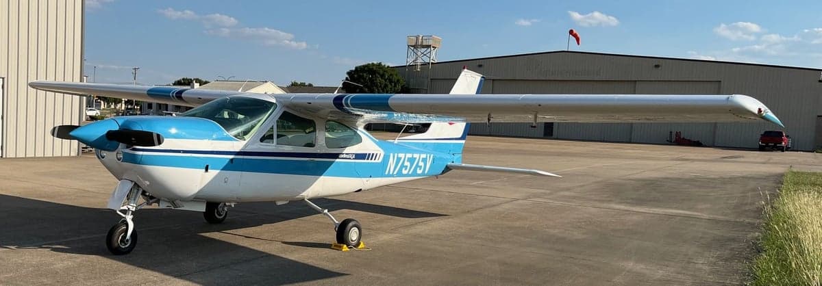 A Cessna Cardinal RG, registration N7575V, parked on the tarmac in front of a hangar.
