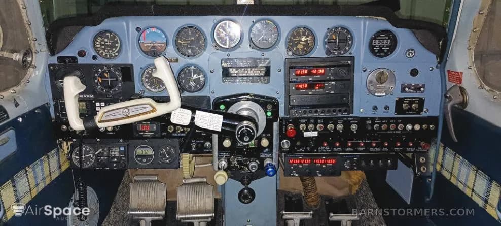 The cockpit of a light aircraft, showing the instrument panel with various gauges, radios, and controls.
