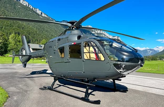 An Airbus helicopter is parked on the tarmac with mountains in the background.