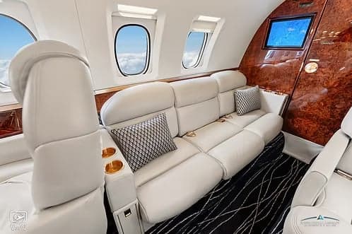 The interior of a jet aircraft with a white leather couch and wood trim.