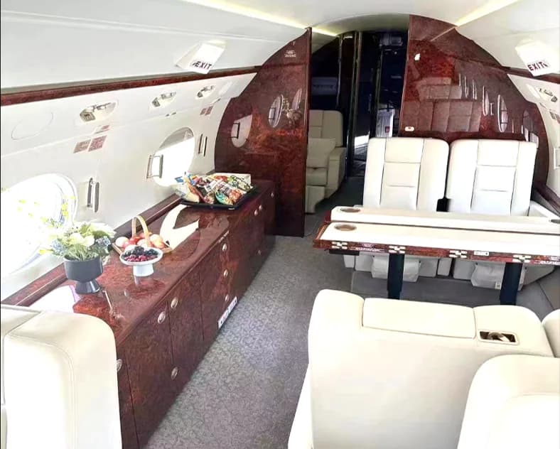 A private jet interior showing a galley area with snacks and a dining table with white leather seats.