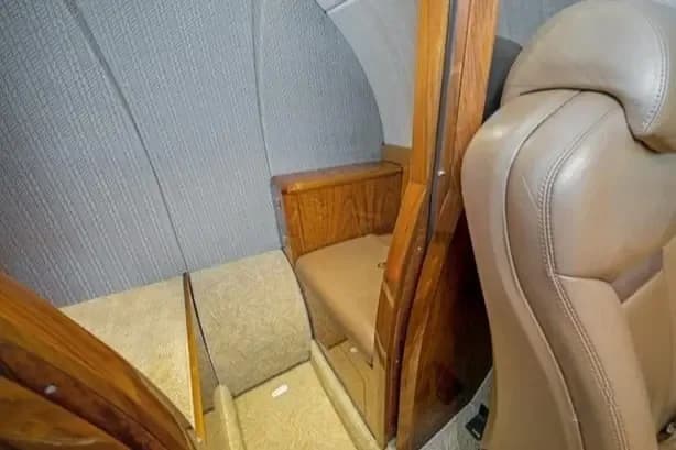 A close-up view of a tan leather seat and a wooden cabinet inside the aircraft cabin.