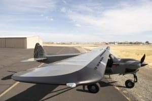 A gray and red Cubcrafters XCub on the tarmac with a hangar in the background.
