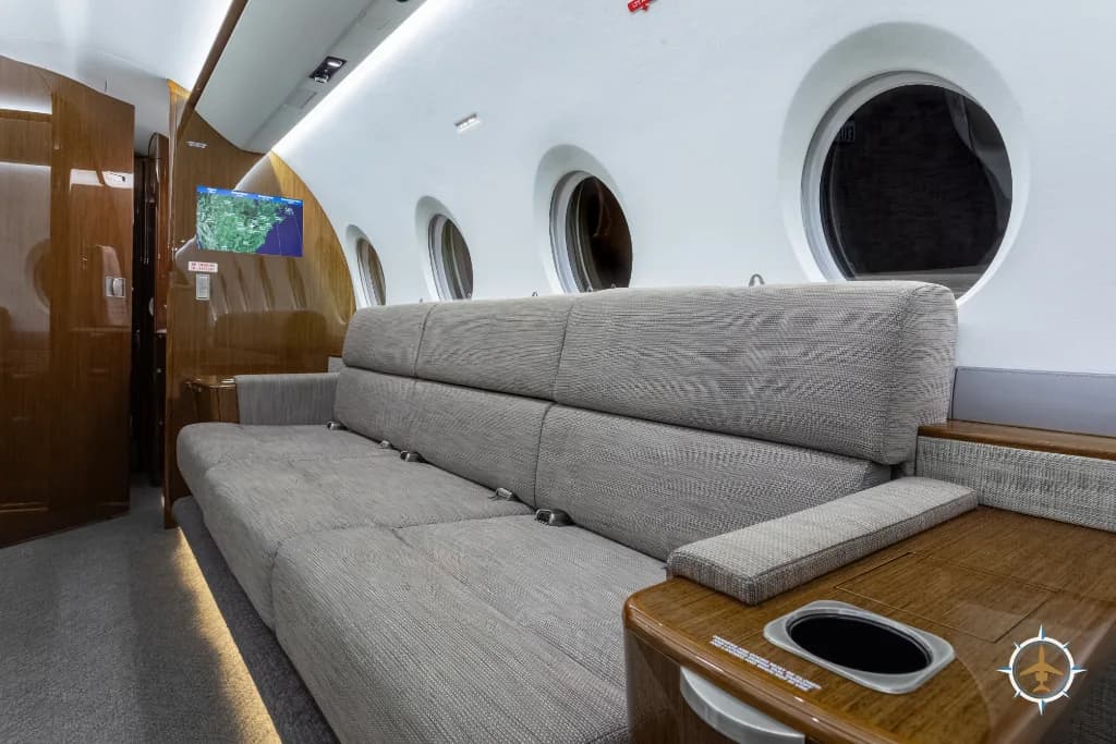 A close-up view of the beige sofa and a wooden side table with a cup holder in the business jet cabin.