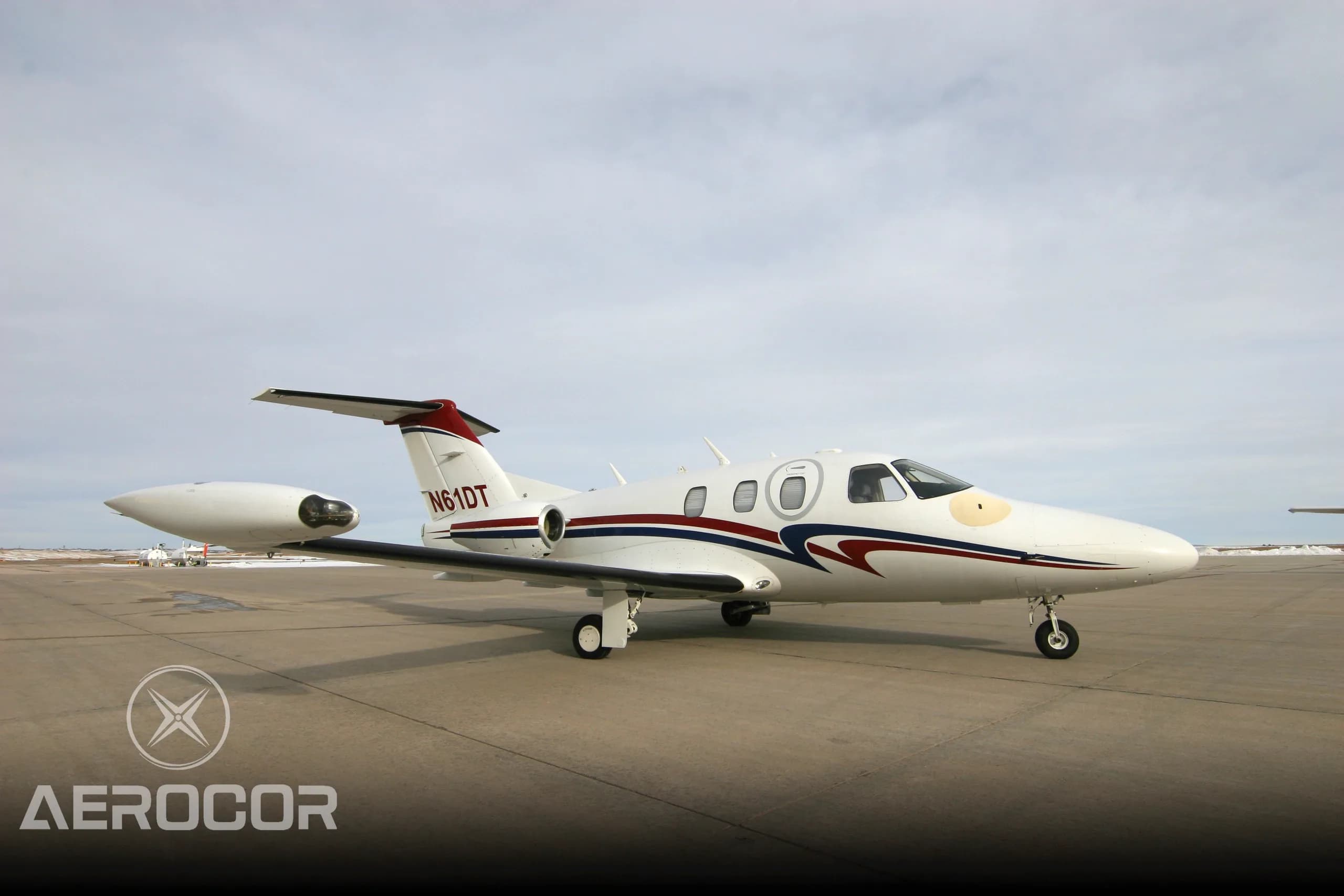 A white Eclipse 500 jet with red and blue stripes parked on an airport tarmac, viewed from the front-right.