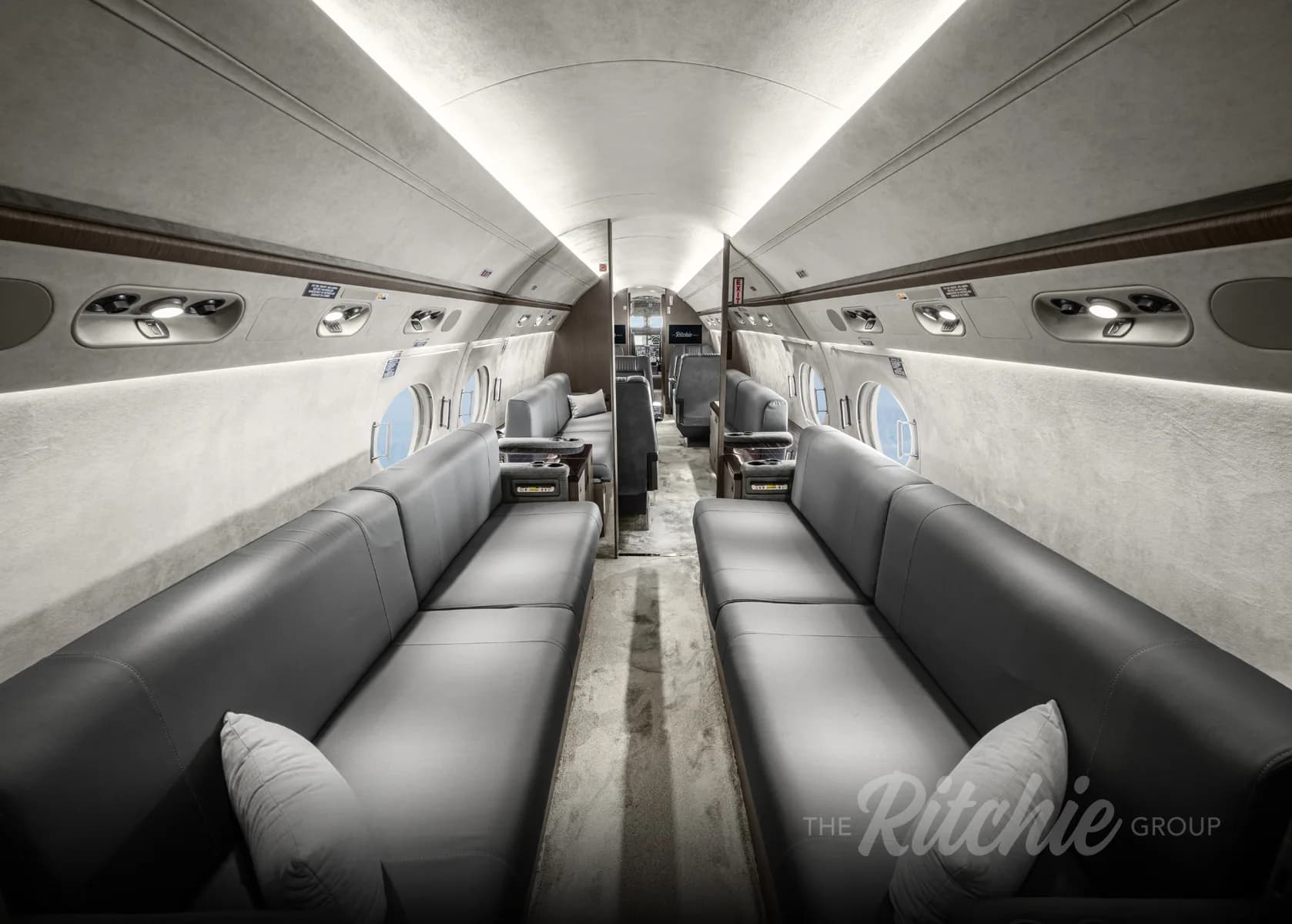 A long view down the aisle of the Gulfstream G650 cabin, showing two rows of grey leather divans.