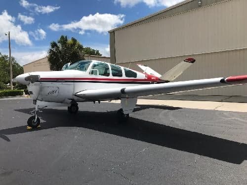 A Beechcraft Bonanza with a white and red paint scheme is parked on the tarmac.