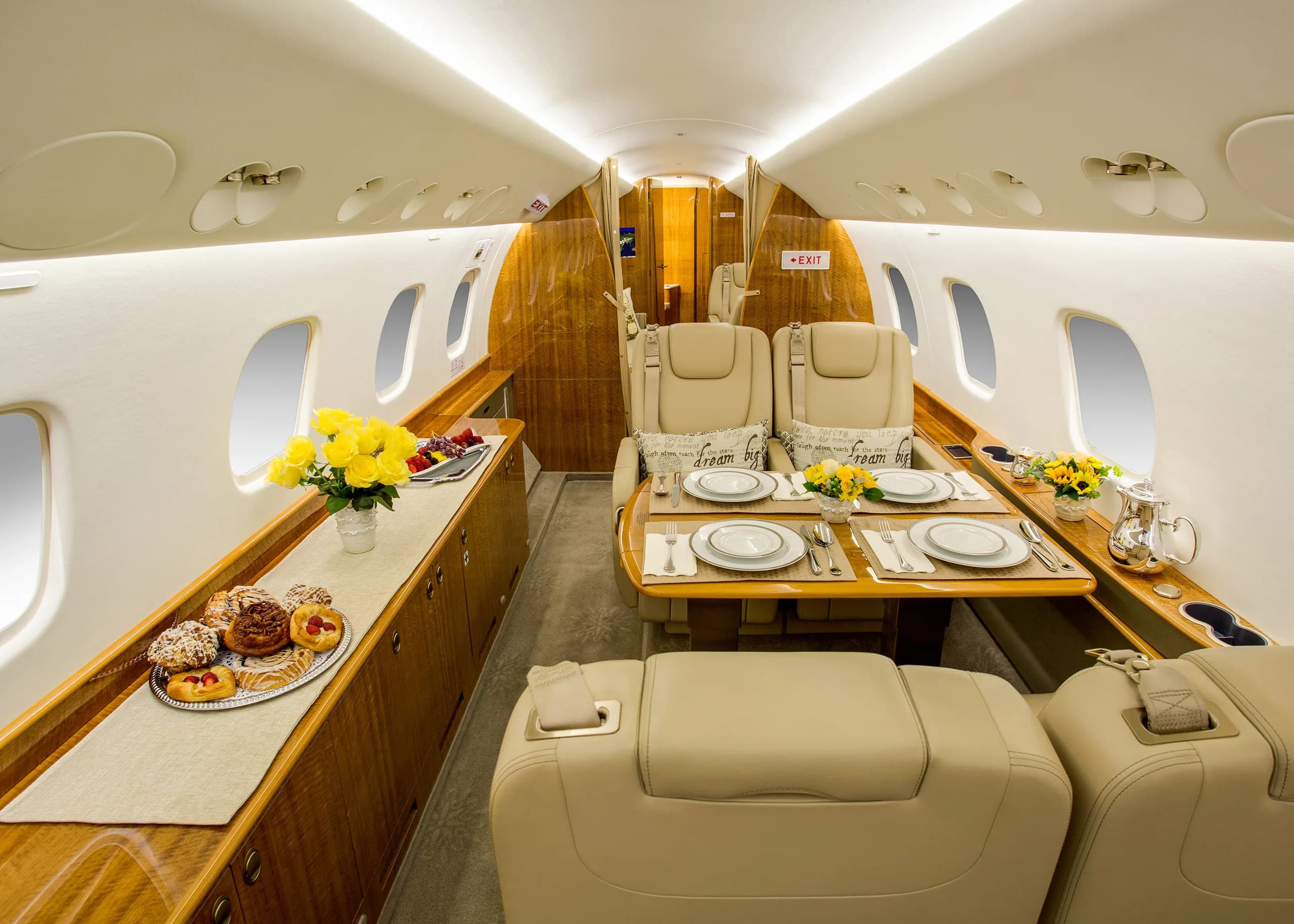 A wide view of a private jet's elegant cabin interior, featuring beige seating, a dining table, and a buffet counter with food.