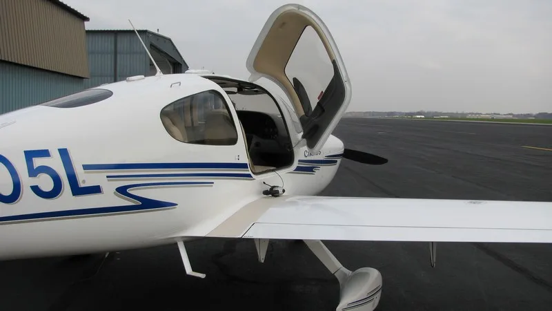 A white Cirrus SR22 aircraft with its doors open, registration N6005L, parked on an airfield.