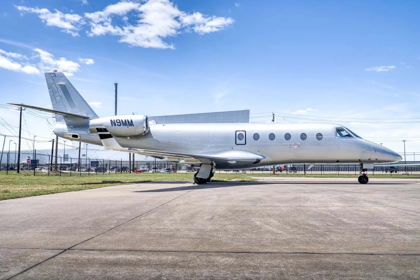 A silver business jet with registration N9MM parked on an airfield, viewed from the side.