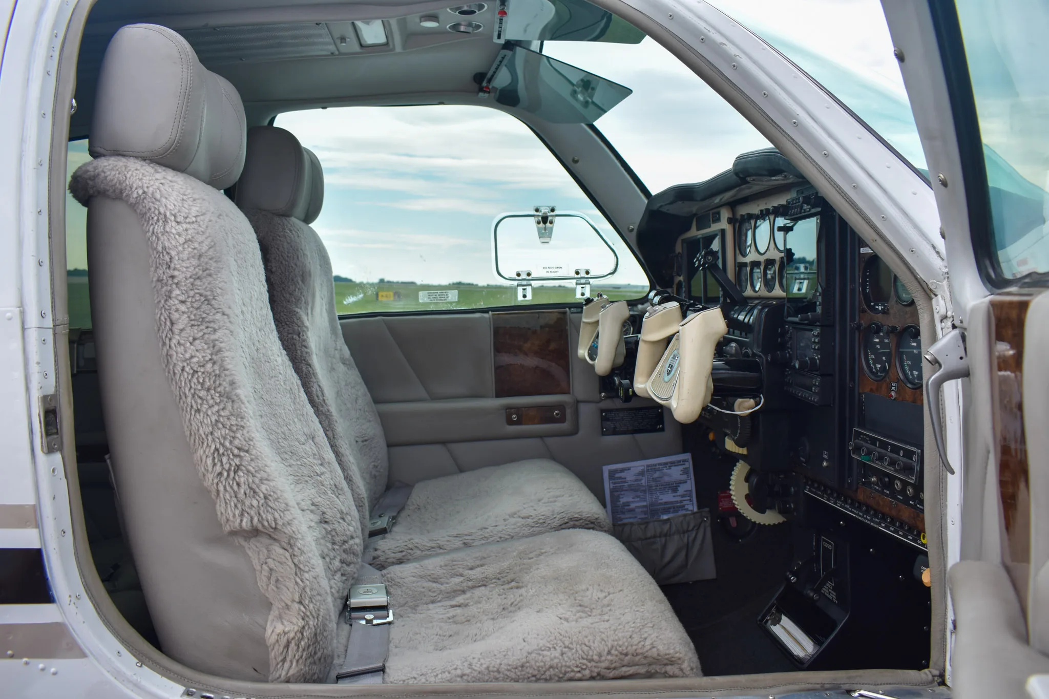 The interior of a Beechcraft Baron cockpit, showing sheepskin-covered pilot and co-pilot seats and part of the instrument panel.