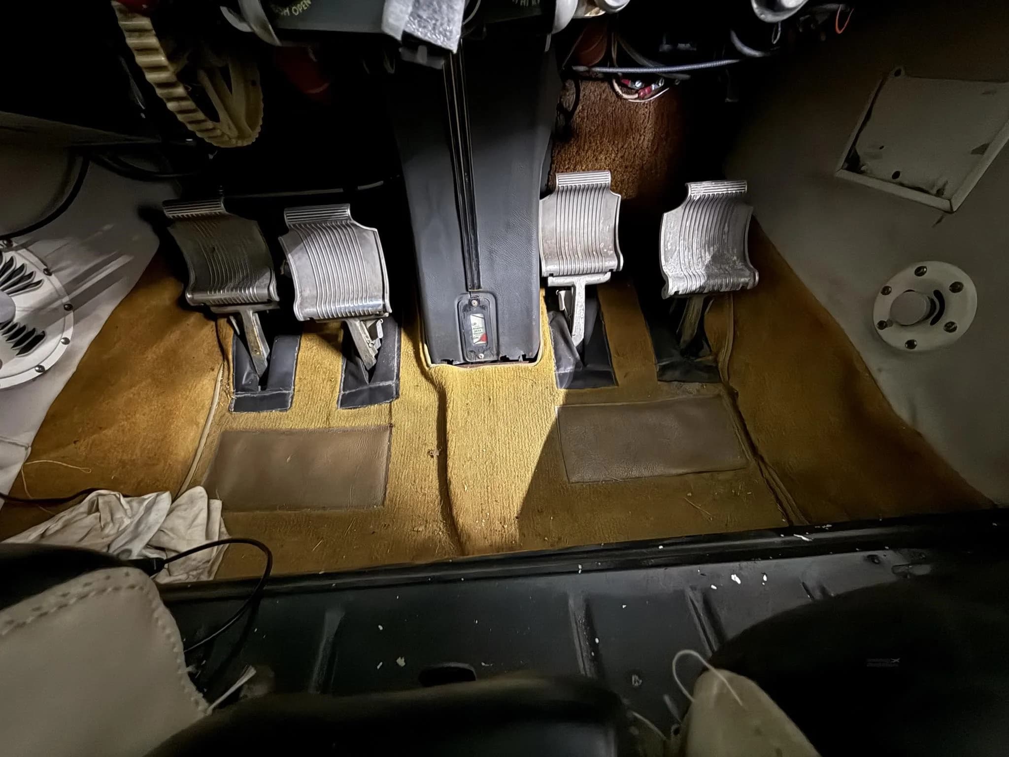 A close-up view of the aircraft's rudder pedals and the tan carpeted floor in the cockpit.