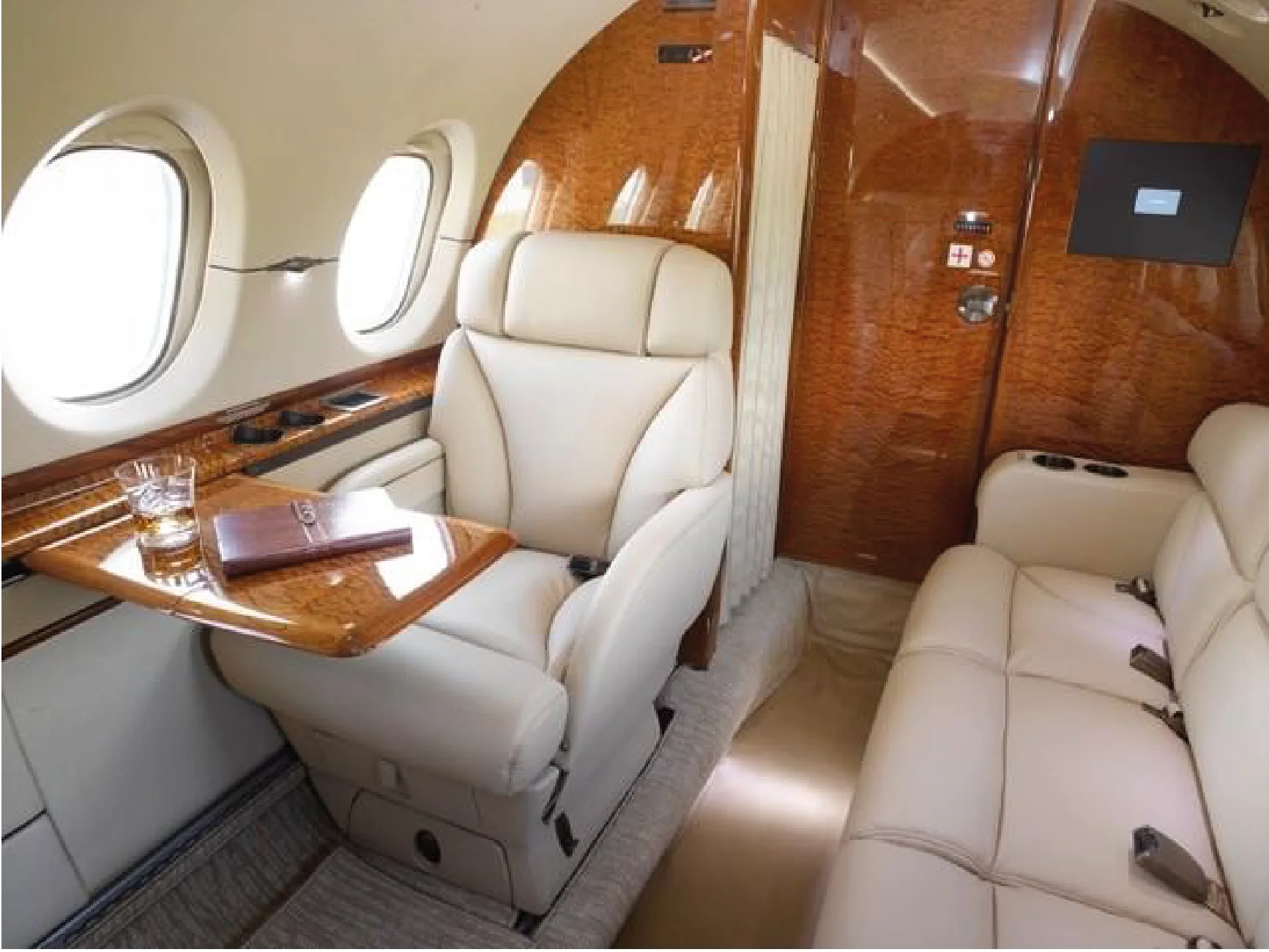 Aircraft interior with cream-colored leather seats, wood trim, and a small table.