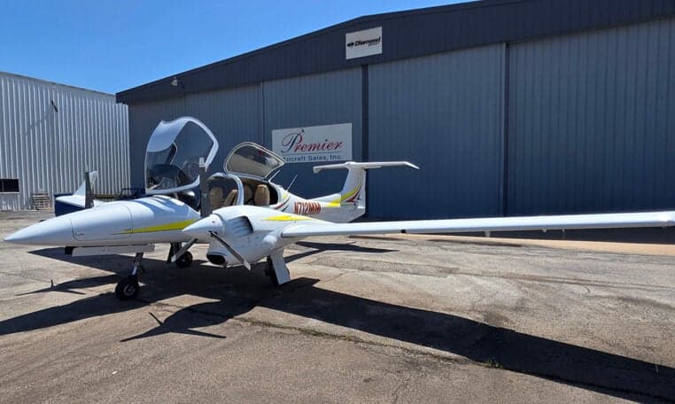 Diamond DA62 aircraft with open gull-wing doors parked in front of a hangar.