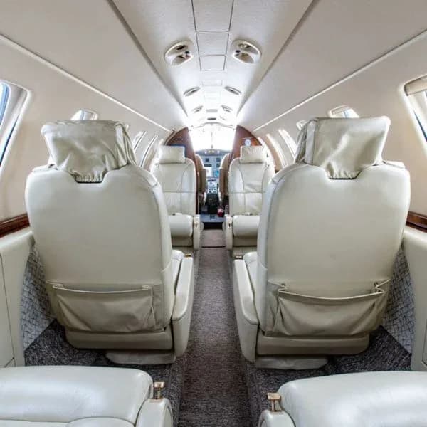 An interior view of an aircraft cabin looking forward towards the cockpit, showing multiple rows of light beige leather seats.