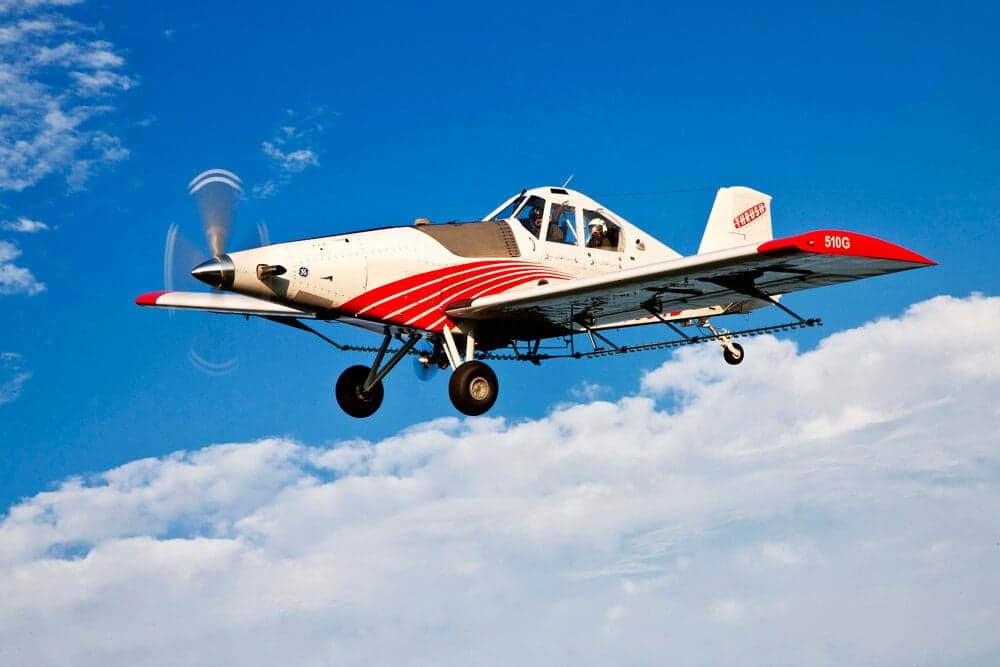 A Thrush 510G aircraft in flight against a blue sky with clouds.